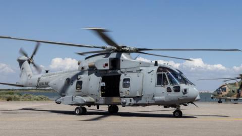 A Merlin Mk4 helicopter in front of a similar model painted in camouflage.  