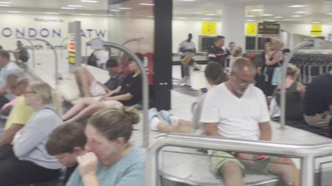 People sit on the luggage carousel at Gatwick Airport