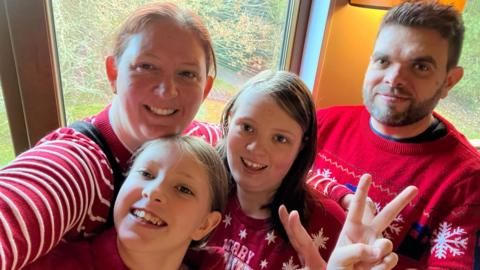 Hannah a'i theulu'n gwenu mewn siwmperi Nadolig