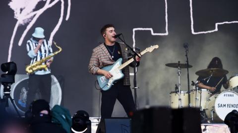Sam Fender holds a blue electric guitar and performs at Glastonbury 2022