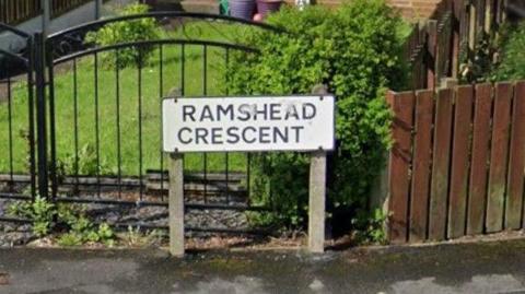 Street View image showing a close-up of a sign saying Ramshead Crescent, with house fences on either side.