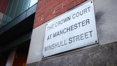 A close-up of a metal sign bolted to a brick wall which states 'The Crown Court at Manchester Minshull Street'