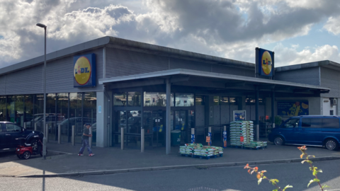 Lidl store with vehicles parked outside and a pile of compost bags outside the doors