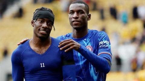 Nicolas Jackson and Noni Madueke together on the pitch after a match - Jackson has his hands on the shoulders of Madueke, who is smiling