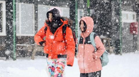 Two people stood in ski jackets while it snows