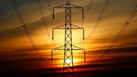 The sun sets behind an electricity pylon 