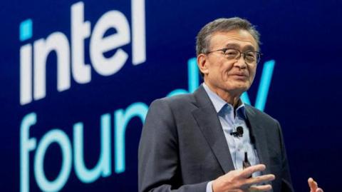 Intel's CEO Lip-Bu Tan speaks at the company's Annual Manufacturing Technology Conference in San Jose, California. Dressed in a dark grey blazer, Mr Tan is standing in front of a blue background with the words "Intel foundry" prominently shown.