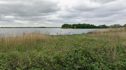 A Google Streetview of a lake with greenery in the foreground.
