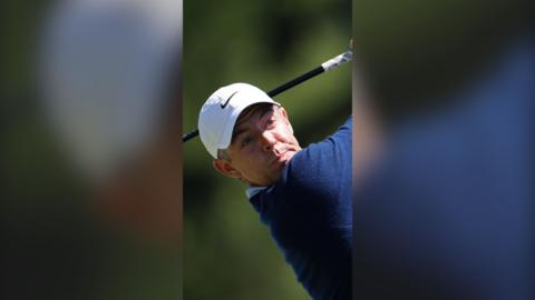 Rory McIlroy wears a white cap and is turned after taking a shot.