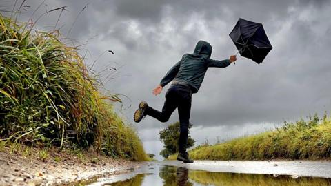 A leaping figure holds on to an umbrella that has been blown inside out