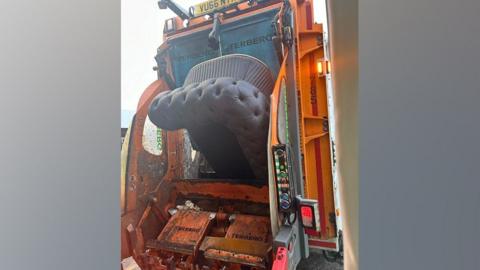 A sofa being loaded into a refuse vehicle.