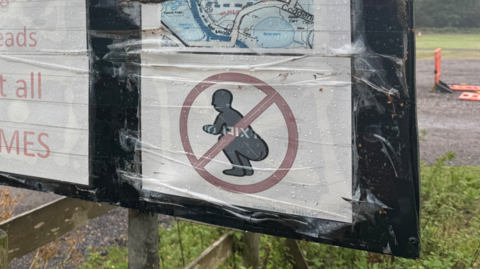 A close-up of a sign showing a figure squatting with a red circle around it. 