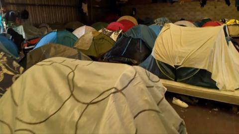 More than a dozen tents inside a warehouse. 