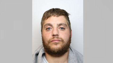 Mugshot of a man with light brown hair and a beard and moustache. He is wearing a grey hoodie and grey top.