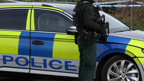 PSNI officer standing in front of a car holding a gun