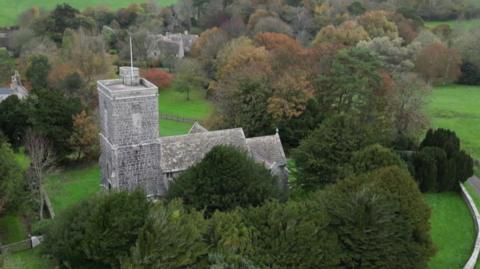 A view from above of an old stone church surrounded by trees and countryside