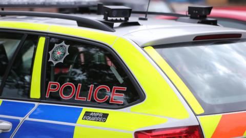 The back of a PSNI-branded car. The word 'POLICE' is on the window alongside the psni badge.