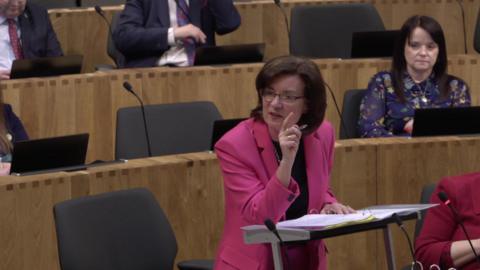 Eluned Morgan on her feet in the Senedd chamber gesticulating with her finger.