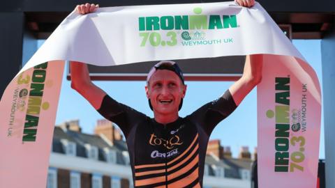 Donald Brooks lifts the banner that lay across the finish line after winning a race in Weymouth