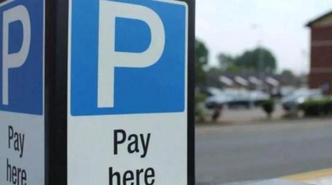 A sign with the letter P and the words pay here. Vehicles and a street are blurred in the background in this generic image.