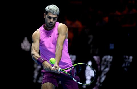 A man wears a sleeveless purple top and is mid shot on a tennis court