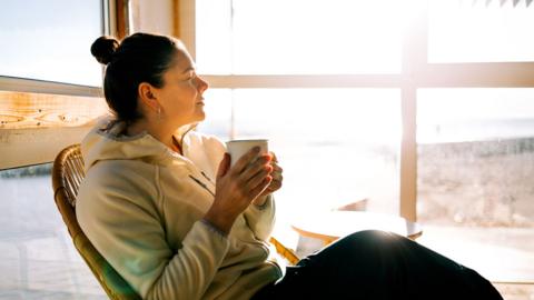 A woman relaxing with warm drink by sunny window