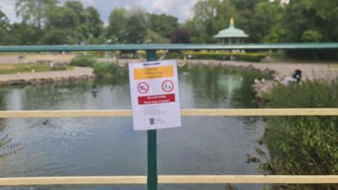 A view of a pond, with fencing around it and a sign telling people to stay away.