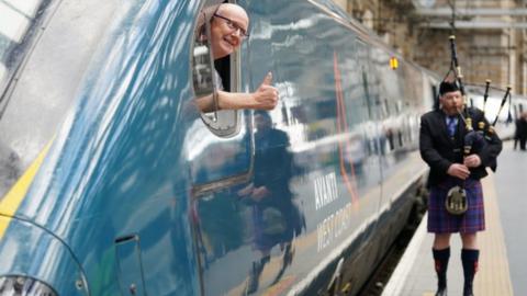 A piper plays as train driver Neil Barker gives a thumbs up from on board the Avanti West Coast Class 390 EMU train which has arrived at Glasgow Central Station from London Euston