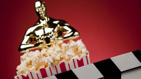 An imitation Oscars statue with some popcorn and a film clapperboard