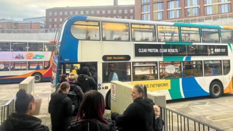 A photograph of passengers boarding the 203 bus service at Stockport Interchange.