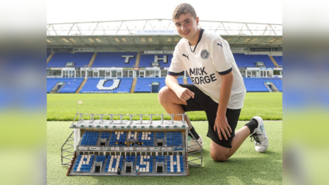 Tom with his Lego project. He is kneeling beside the pitch at the Weston Homes Stadium