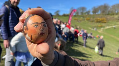 A hand holds an egg painted to resemble Frida Kahlo.