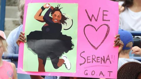 A fan holds a sign saying 'We love Serena GOAT'