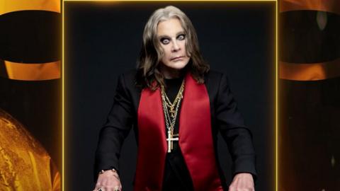 A photo of Ozzy Osbourne wearing a black jacket with large red lapels and several gold chains with crosses around his neck. He looks intensely at the camera.