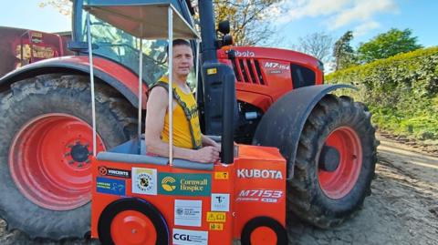 Michael Barrett stands in front of a red Kubota tractor, wearing a tractor costume that looks very similar