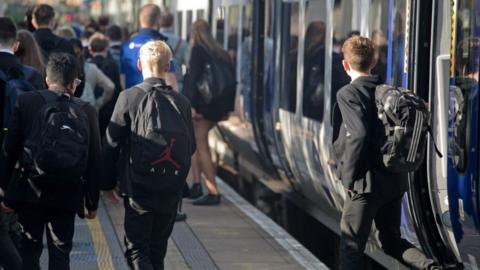 School children at a railway station, having just alighted a train. They are wearing black blazers. 