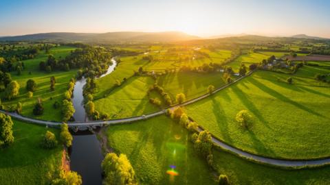 Sunset illuminating green pasture, agricultural crops, farms, villages and the distant mountains beyond the River Usk