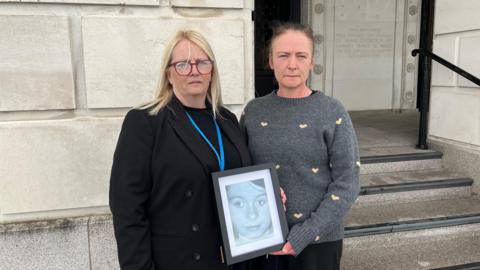Lisa Morris, left, and Roisin Morris, right, pictured outside Parliament Buildings, Stormont, holding a photograph of their mother Madeline