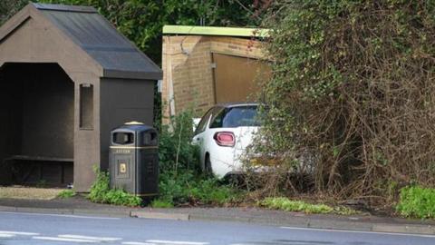 An image of the site in Pagham Road, near Nyetimber, where a car crashed into a gas substation. A white car can be seen crashed into the substation building, which is just beside a brown bus stop.