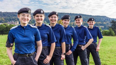 Six girls - aged 14 and 15 - stood in a diagonal line on a field wearing police cadet uniform 