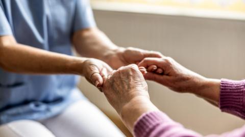 Stock close-up image of a nurse holding an elderly person's hands.