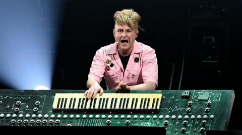 A man stand behind a large keyboard built into what appears to be a large circuit board.