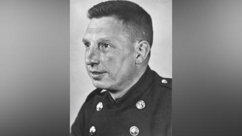 A black and white head and shoulders photograph of a Sheffield firefighter wearing a traditional uniform