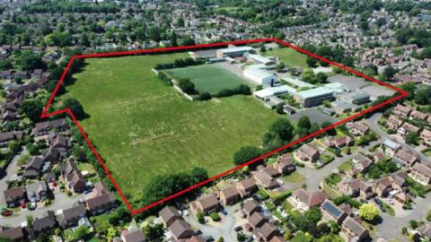An aerial view of the former Kenilworth School site with a red line showing the outline of the site which includes buildings and a large green space. 