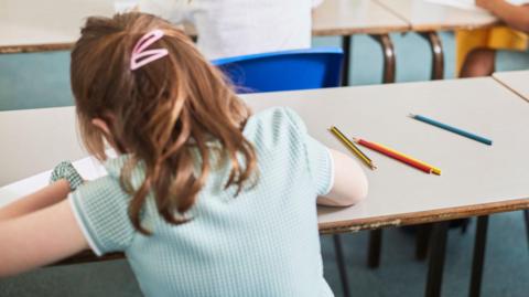 Schoolgirl writing at classroom desk in primary school lesson.