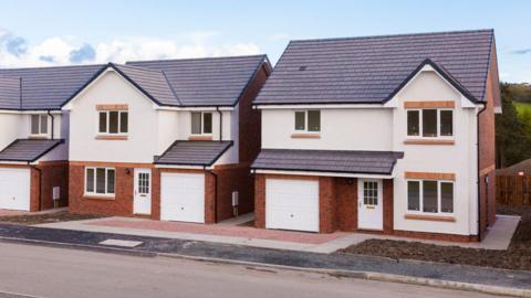 Three newly-built detached houses with red brick on the ground floor, a garage and painted white at the top floor