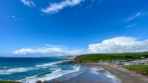 Waves coming into a wide beach below blue sky and white cloud