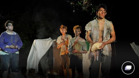 A photograph from the Lord of the Flies play. There are a group of young boys in disheveled clothes.