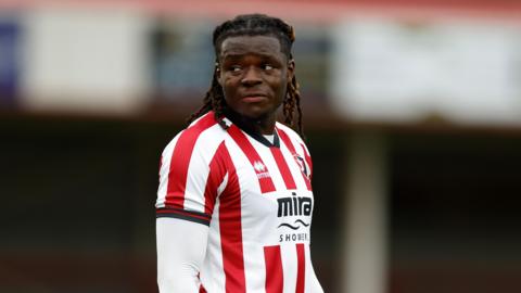 Ibrahim Bakare standing on the pitch with his arms by his side during a pre-season match for Cheltenham