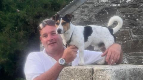 James Southey looking and smiling at the camera with his small dog stood on a wall.